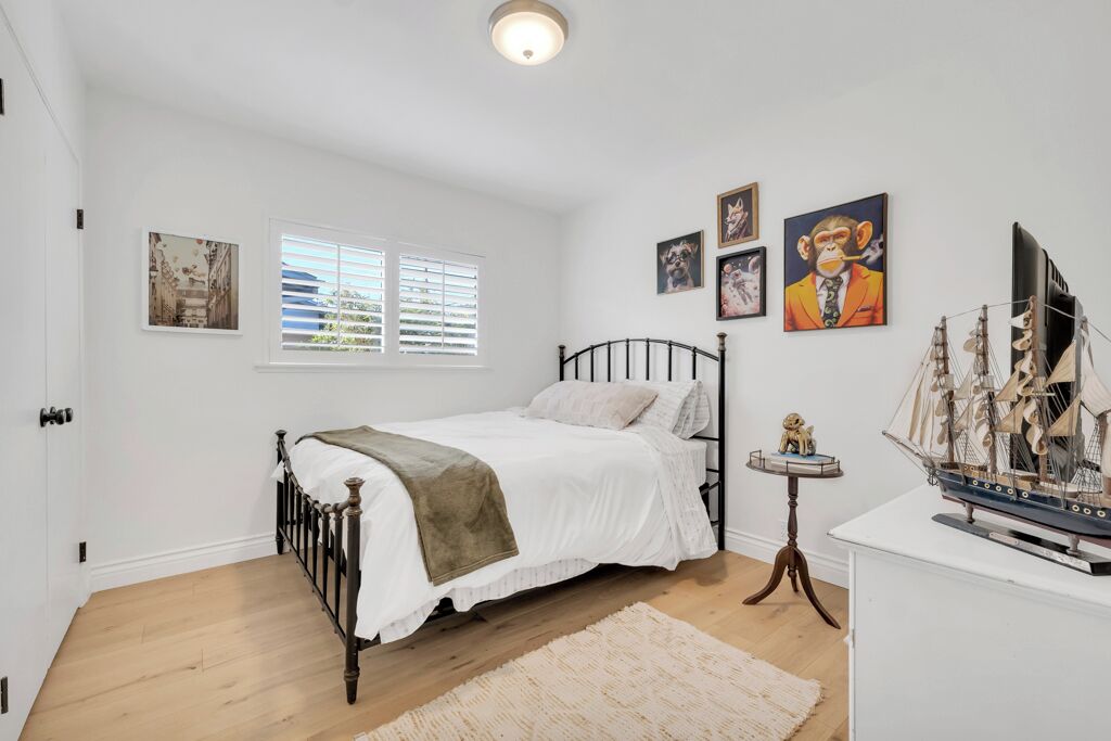 A bedroom with a bed, a small table with a ship model, and wall art.