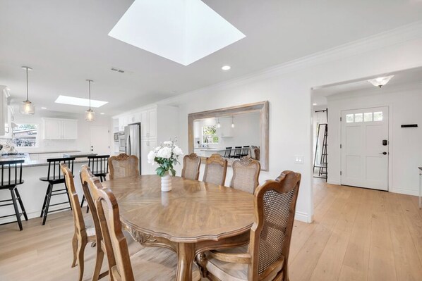 A spacious dining area with a large wooden table and chairs, a skylight, and white cabinetry.