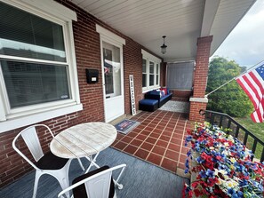 Eine überdachte Terrasse mit einer Ziegelwand, einem weißen Metalltisch und -stuhl, einem blauen Sofa und einer US-amerikanischen Flagge.