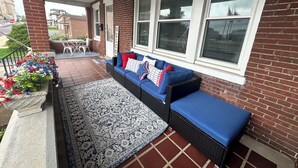 A covered porch with a blue sofa, a patterned rug, and a flower planter.