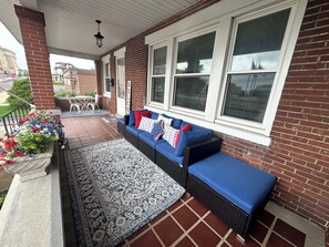 A covered porch with a blue sofa, a patterned rug, and a flower planter.