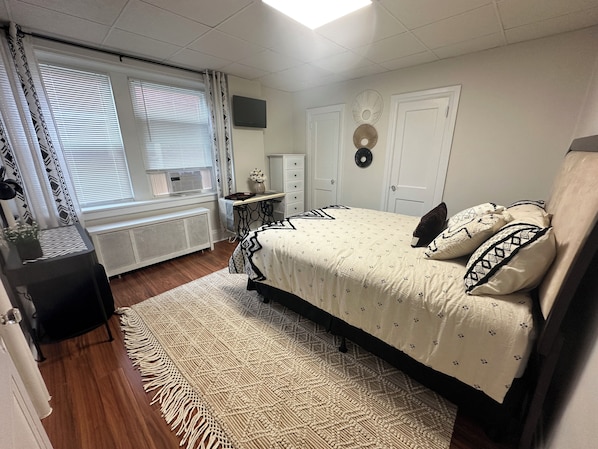 A bedroom with a bed, bedside table, dresser, radiator, and a window with curtains.