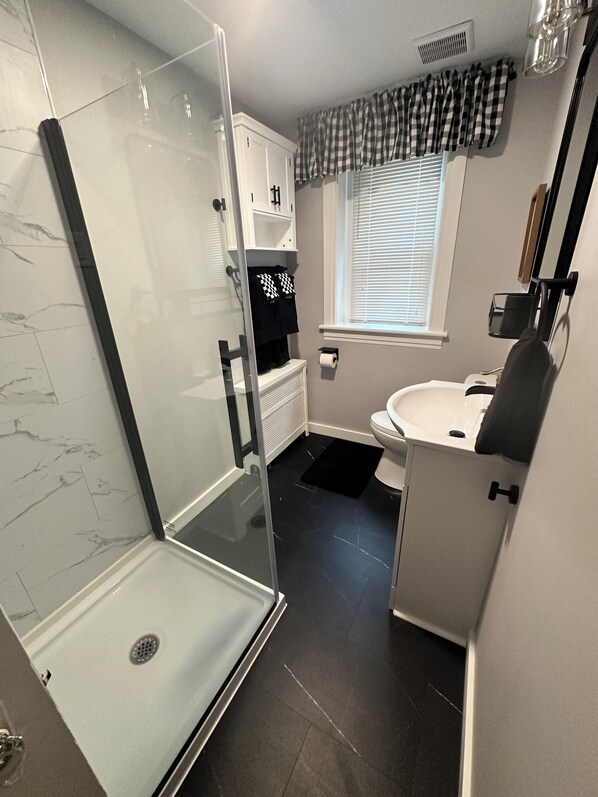 A bathroom with a glass shower enclosure, a white sink, and a toilet.
