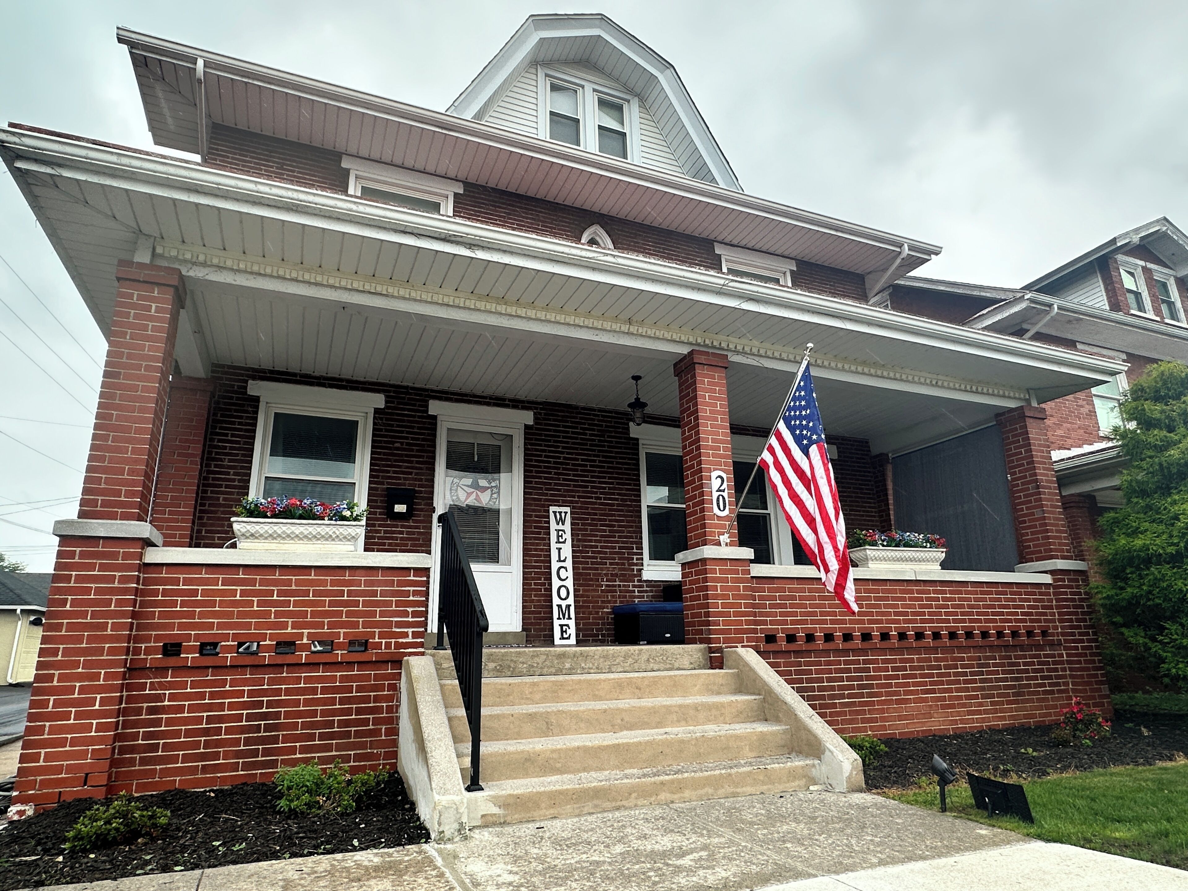 A two-story house with a front porch, a welcome sign, and an American flag.