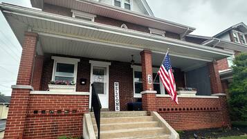 A two-story house with a front porch, a welcome sign, and an American flag.