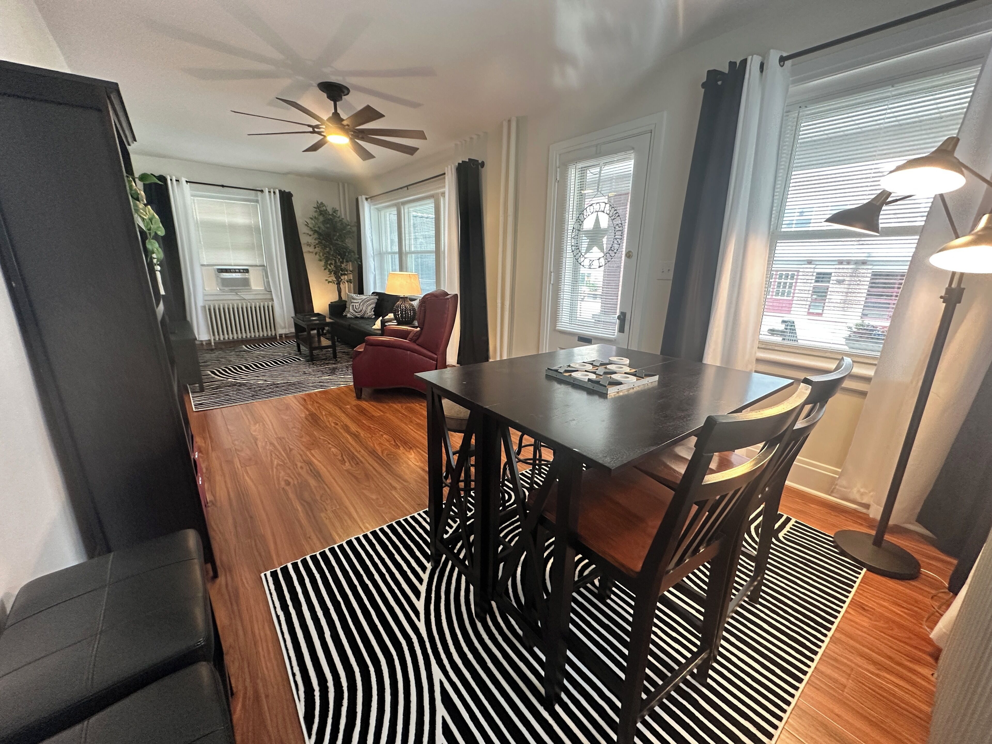 A dining area with a table, chairs, a ceiling fan, and a view of the outside through large windows.