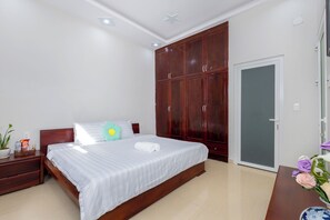 A bedroom with a bed, wooden wardrobe, bedside table, and a door.