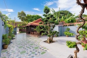 A courtyard with a tiled floor, a covered seating area, and various potted plants.