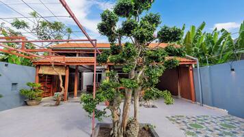 A residential property with a covered patio area, a house with a tiled roof, and a garden with a central tree.