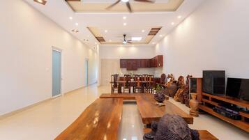 A spacious living room with a wooden dining table, a ceiling fan, recessed lighting, and a kitchen area in the background.