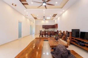 A spacious living room with a wooden dining table, a ceiling fan, recessed lighting, and a kitchen area in the background.