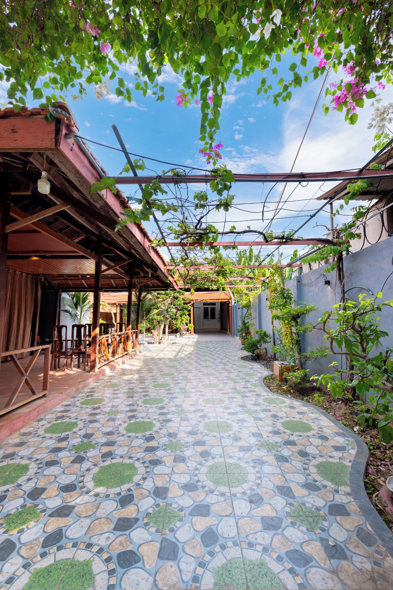 Un espace extérieur abrité, doté d’un sol carrelé, de meubles en bois et de plantes.