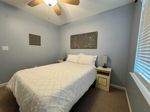 Ein Schlafzimmer mit einem Bett, zwei Nachttischen, einem Deckenventilator und Wanddekoration.