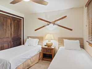 Ein Hotelzimmer mit zwei Betten, einem Nachttisch aus Holz mit Lampe und einem Deckenventilator.