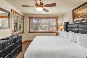 A bedroom with a bed, a dresser, a ceiling fan, a window with blinds, and a lamp.