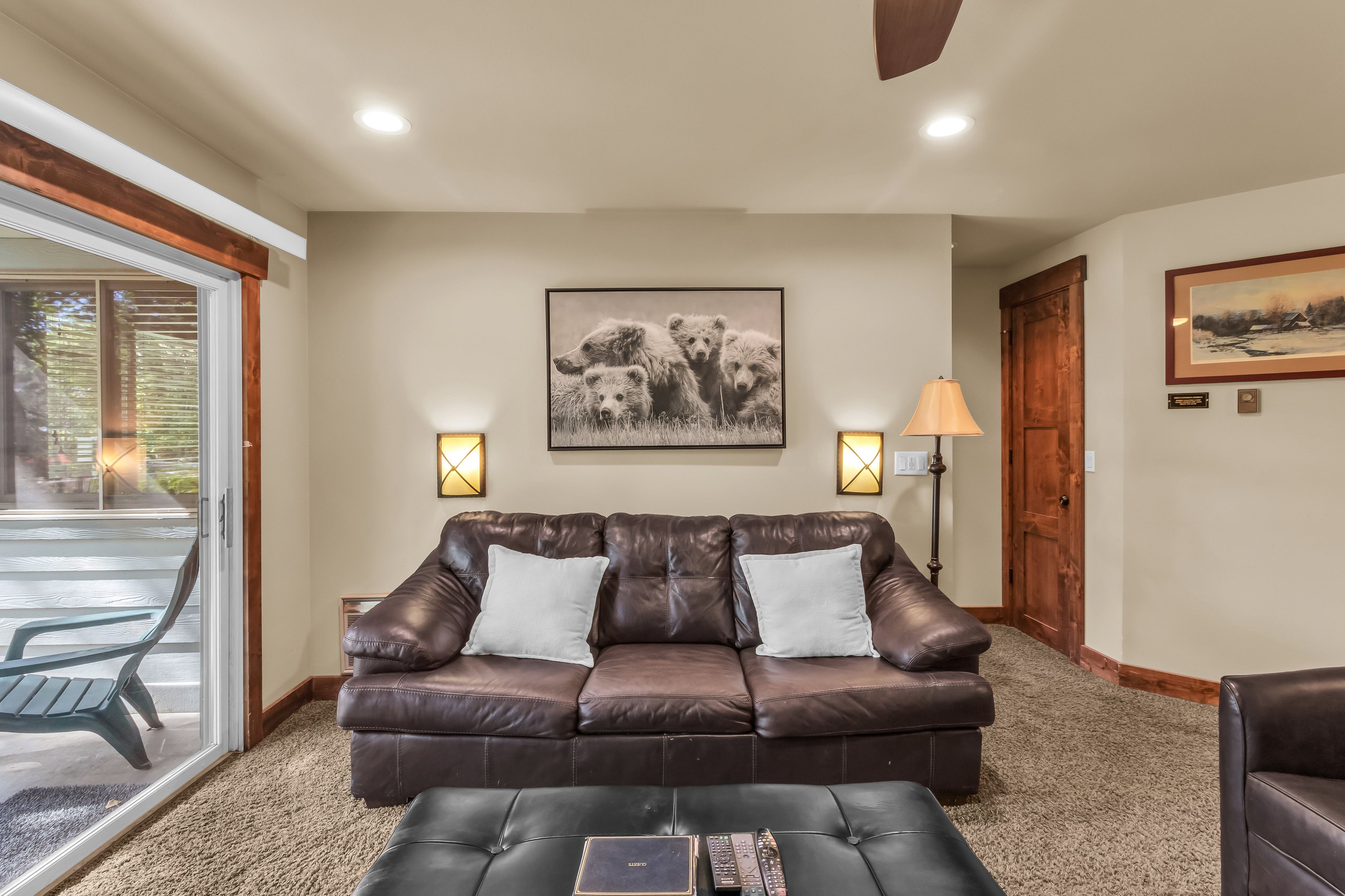 A living room with a brown leather sofa, two white cushions, a coffee table, and a painting of bears on the wall.