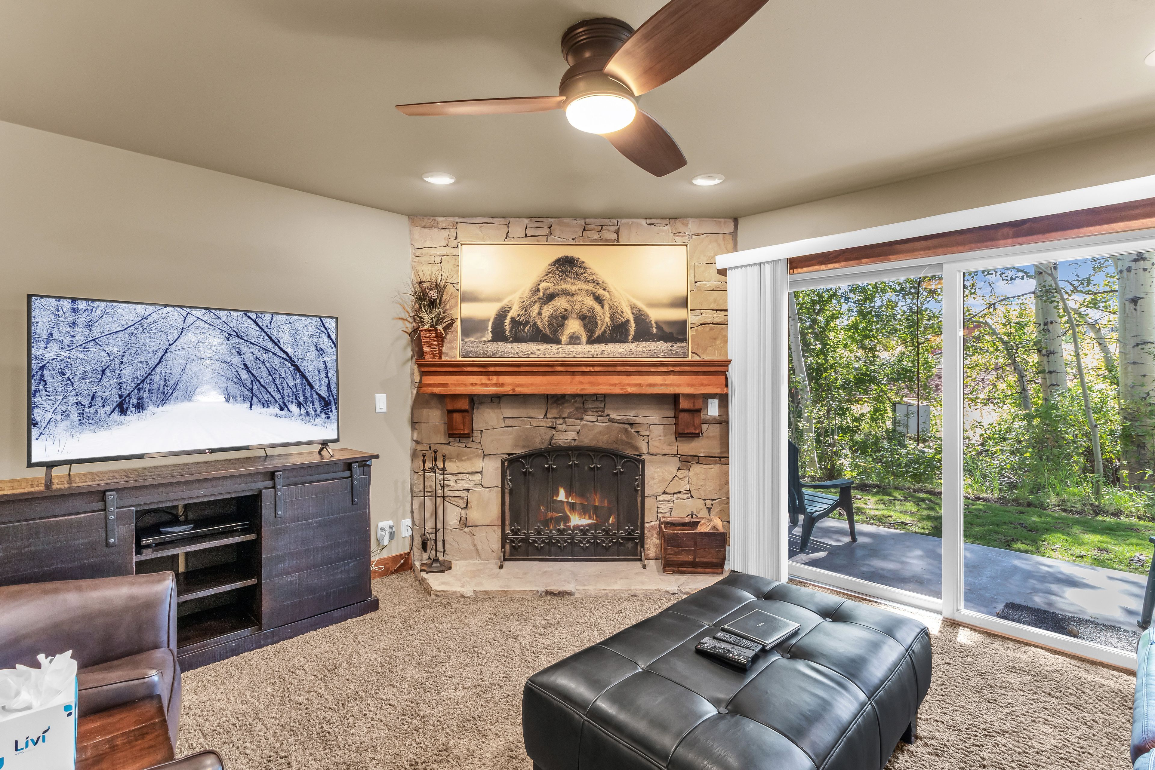 Una sala de estar con chimenea de piedra, televisor y ventana grande con vista a un jardín.