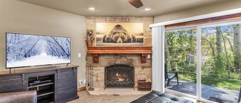 Una sala de estar con chimenea de piedra, televisor y ventana grande con vista a un jardín.