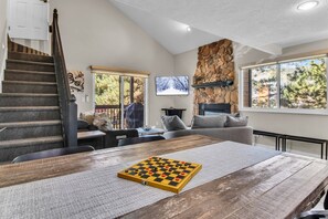A modern living room with a fireplace, a large window, and a wooden table with a chessboard. - Red Pine V6 | Canyons Village | Pools | Hot Tub | Sleeps 8 (Park City)