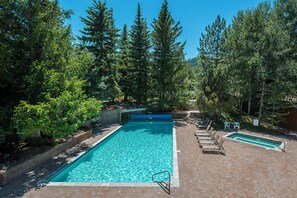 Une piscine rectangulaire à l’eau d’un bleu limpide, entourée d’une terrasse en briques et de chaises longues en bois.