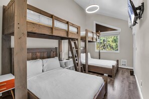 Une chambre avec un lit superposé, une échelle, un bureau et une fenêtre donnant sur un paysage verdoyant.