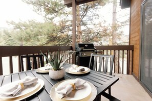 Eine Holzterrasse mit Tisch für Zwei, einem Grill und einem Blumentopf.