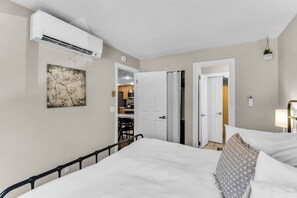 A hotel room with a bed, a bedside table, a wall-mounted air conditioner, a painting, and a view into the kitchen area. - Red Pine V6 | Canyons Village | Pools | Hot Tub | Sleeps 8 (Park City)