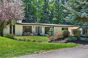 A modern two-story house with a covered patio, surrounded by a well-maintained garden and tall evergreen trees. - Hulen Hideaway | Hot Tub | Perfect Location (Ketchum)