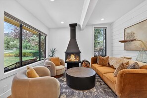 A modern living room with a fireplace, large windows, and a cozy seating area. - Hulen Hideaway | Hot Tub | Perfect Location (Ketchum)