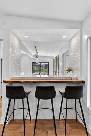 A modern kitchen with a central island, bar stools, and a view of the outdoors. - Hulen Hideaway | Hot Tub | Perfect Location (Ketchum)
