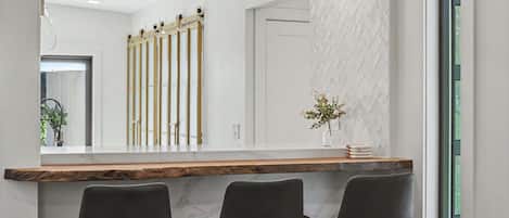 A modern interior with a wooden counter, three black chairs, and a large mirror reflecting the room.