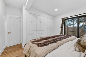 Een slaapkamer met een bed, een kledingkast, een deur en een raam met gordijnen.