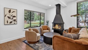 A modern living room with a fireplace, comfortable seating, and large windows. - Hulen Hideaway | Hot Tub | Perfect Location (Ketchum)