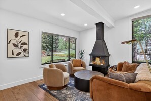 A modern living room with a fireplace, comfortable seating, and large windows. - Hulen Hideaway | Hot Tub | Perfect Location (Ketchum)