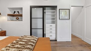 A bedroom with a bed, a wardrobe with sliding doors, a shelf with decorative items, and a framed picture on the wall. - Hulen Hideaway | Hot Tub | Perfect Location (Ketchum)