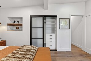 A bedroom with a bed, a wardrobe with sliding doors, a shelf with decorative items, and a framed picture on the wall. - Hulen Hideaway | Hot Tub | Perfect Location (Ketchum)