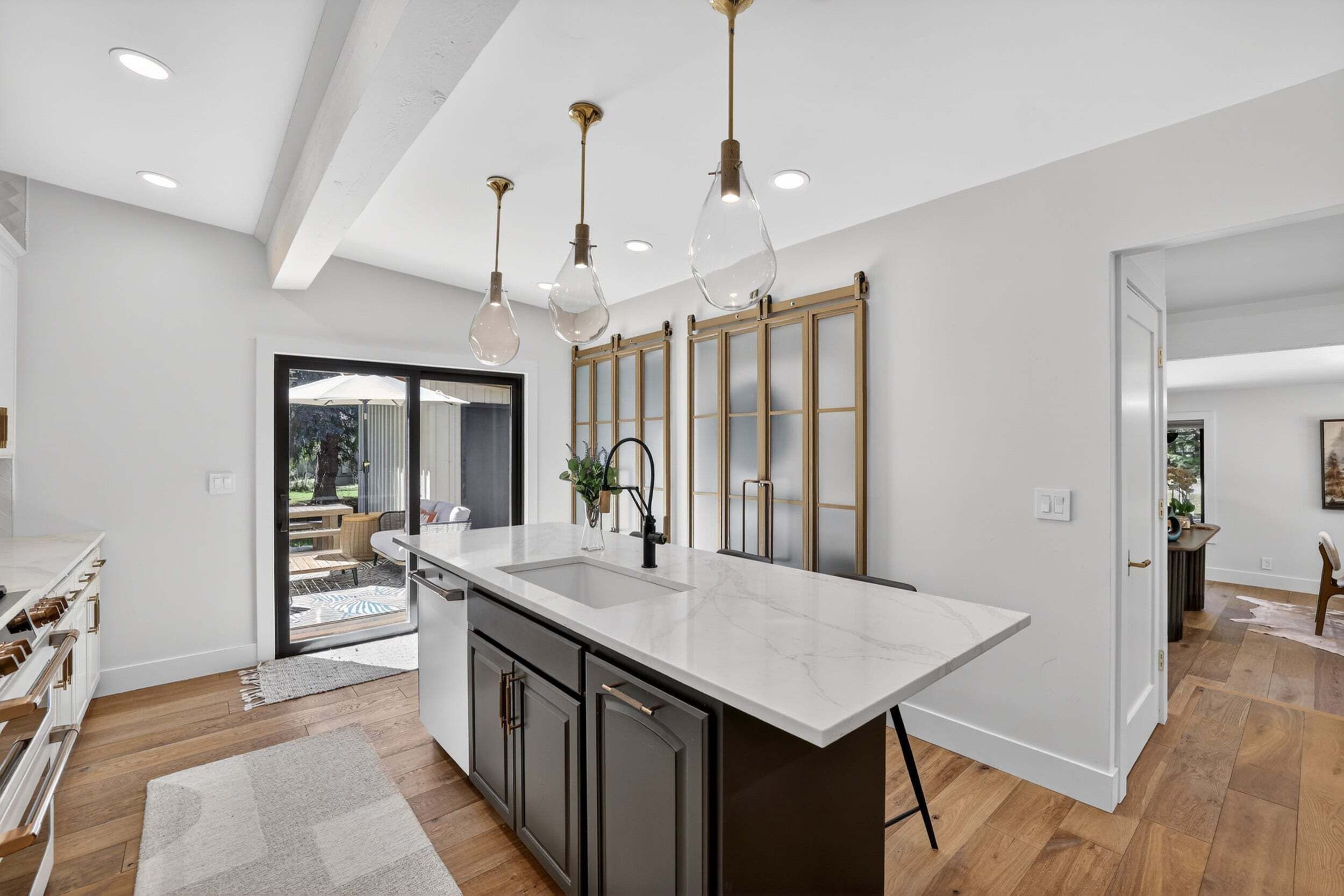 A modern kitchen with a large island, pendant lighting, and a view to the outdoor patio.