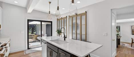 A modern kitchen with a large island, pendant lighting, and a view to the outdoor patio.