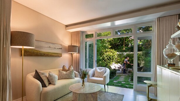 A modern living room with a sofa, coffee table, and lamps. There is a large window with a view of a garden. - Breathtaking Views & Tranquil Luxury at Mont Rochelle, 1027 (Western Cape)