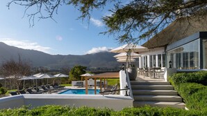 A pool area with lounge chairs, a pergola with umbrellas, and a view of mountains. - Breathtaking Views & Tranquil Luxury at Mont Rochelle, 1027 (Western Cape)