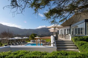 Ein Poolbereich mit Liegestühlen, einer Pergola mit Sonnenschirmen und Blick auf Berge.
