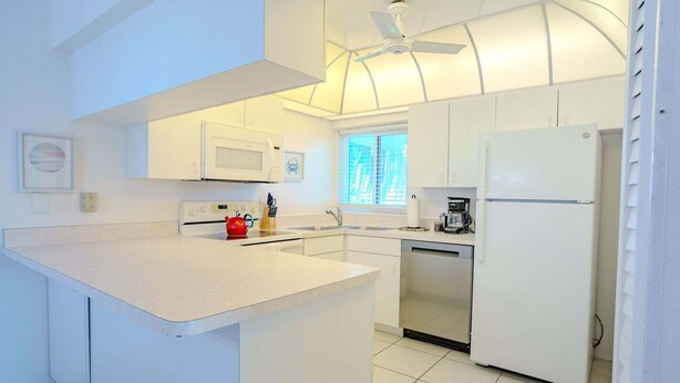 Una cocina moderna con armarios blancos, una isla central, microondas, cafetera y lavavajillas.