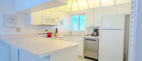 Une cuisine moderne avec des meubles blancs, un îlot central, un four à micro-ondes, une machine à café et un lave-vaisselle.