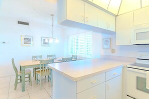A kitchen with white cabinets, a central island, a dining table with chairs, and a microwave. - Two Bedroom Siesta Beach Condo with a view (Sarasota)