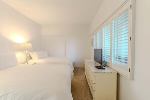 Quarto de hotel com duas camas, uma escrivaninha com televisão e uma janela com persianas.
