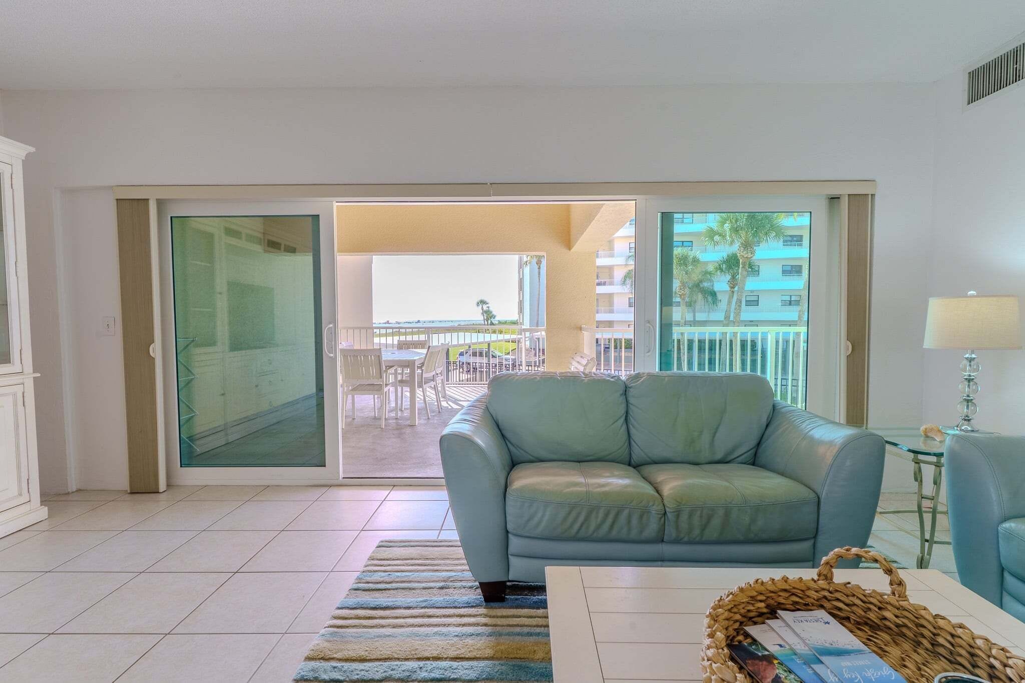 A living room with a sofa, a coffee table, a lamp, and a view of a balcony with outdoor furniture.