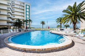 A swimming pool with a surrounding deck, palm trees, and a view of the ocean. - Two Bedroom Siesta Beach Condo with a view (Sarasota)