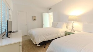 Habitación de hotel con dos camas, un escritorio con una computadora, una lámpara y una puerta que da a otra habitación.