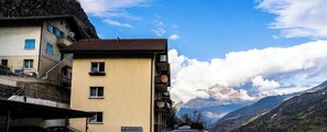 A multi-story building with balconies, a mountain backdrop, and a clear sky.