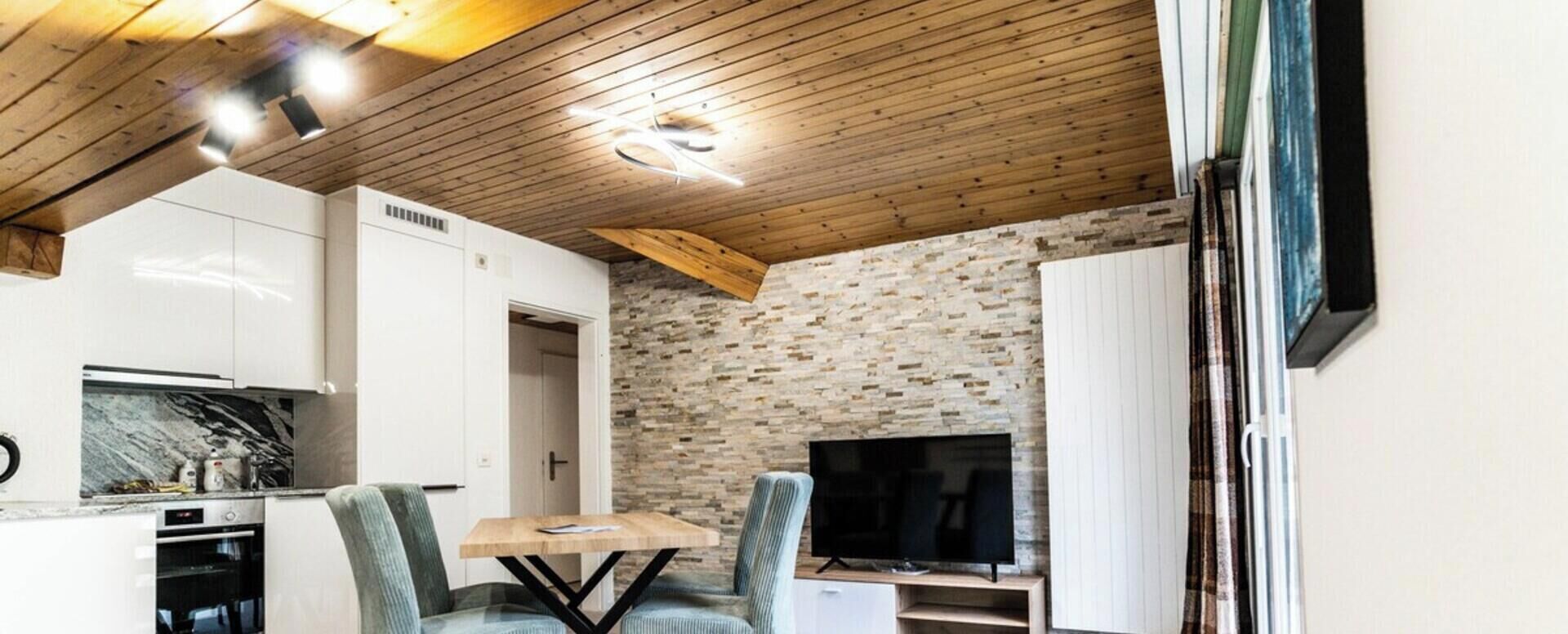 A modern kitchen with white cabinets, a built-in oven, and a dining area with a table and chairs.